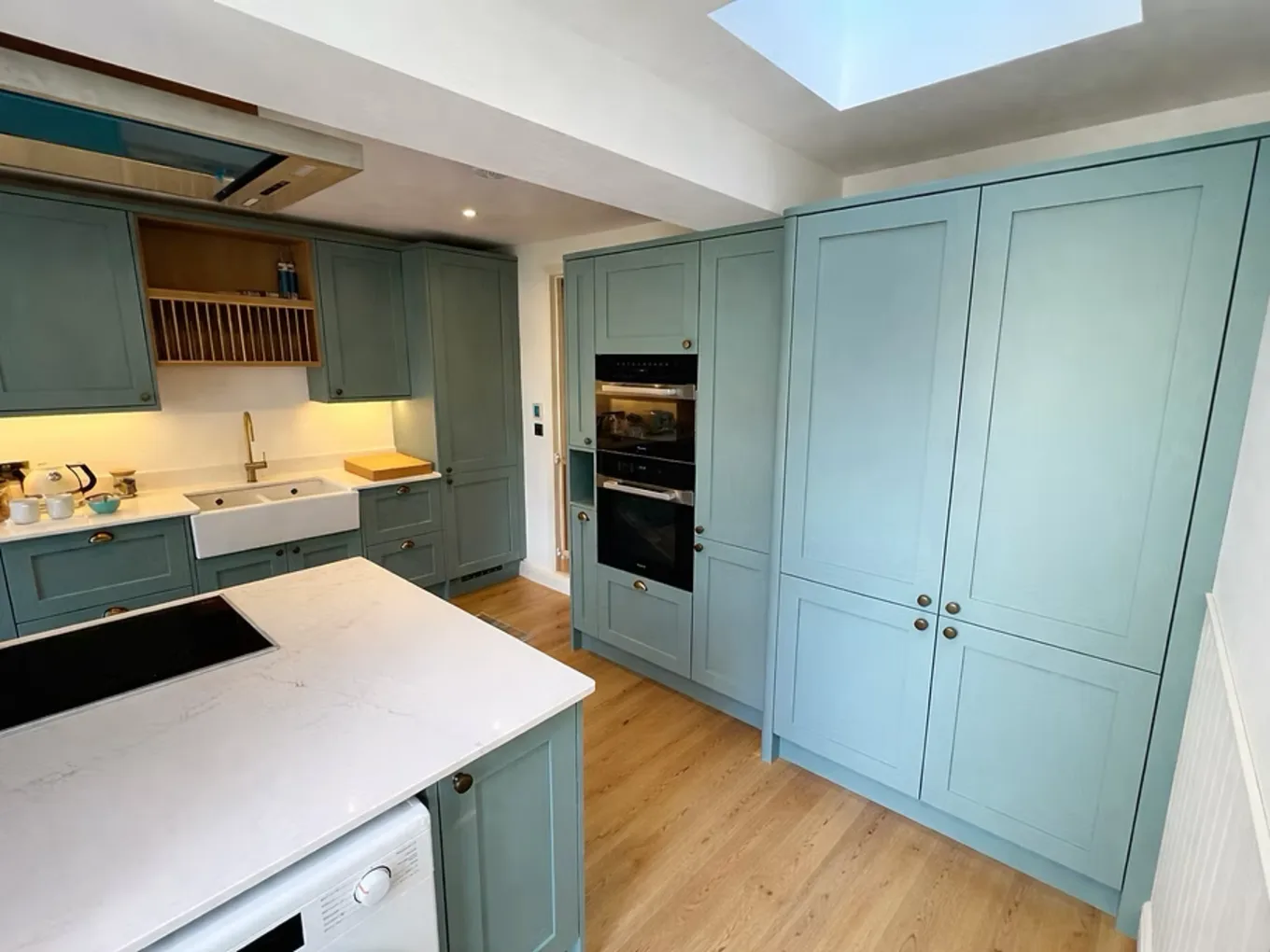 Bespoke sage-green shaker kitchen with brass hardware and white quartz worktops