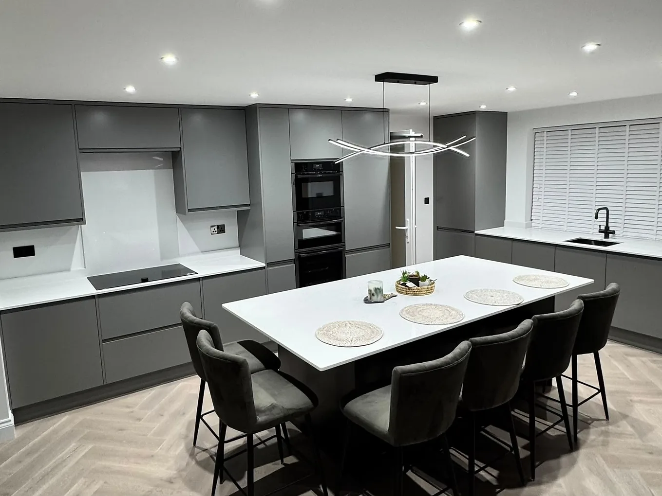 Handleless matte grey kitchen with a large island, black Neff double oven and a herringbone oak floor