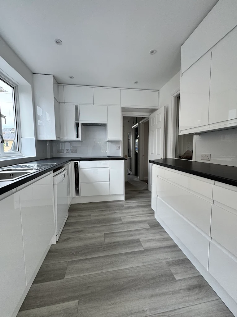 Compact galley kitchen with high-gloss white handleless cabinetry, dark worktops and glass splashback