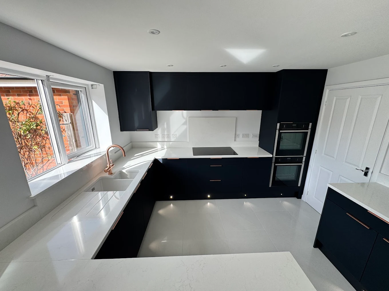 Recently completed dark navy kitchen with copper handles and a white quartz island