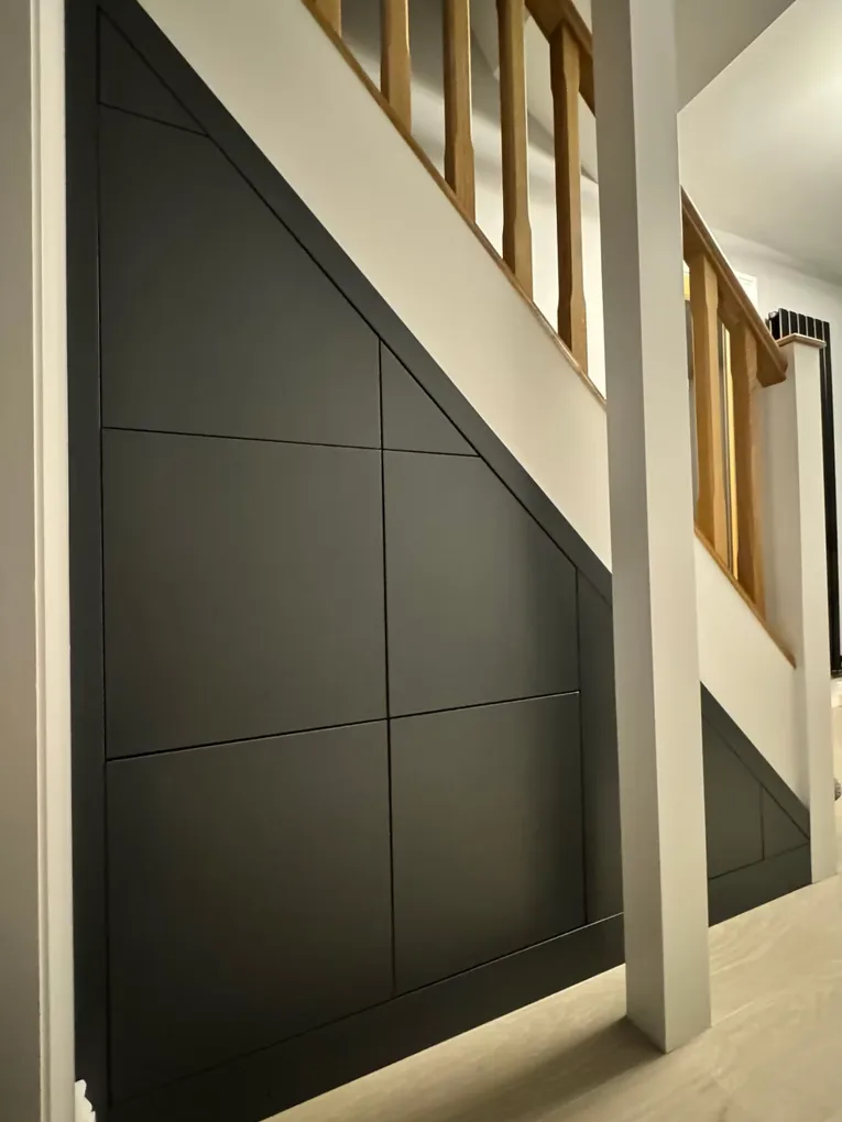 Bespoke under-stair storage cupboard in dark charcoal panelling, built to follow the exact angle of the staircase above, with oak spindles and handrail visible